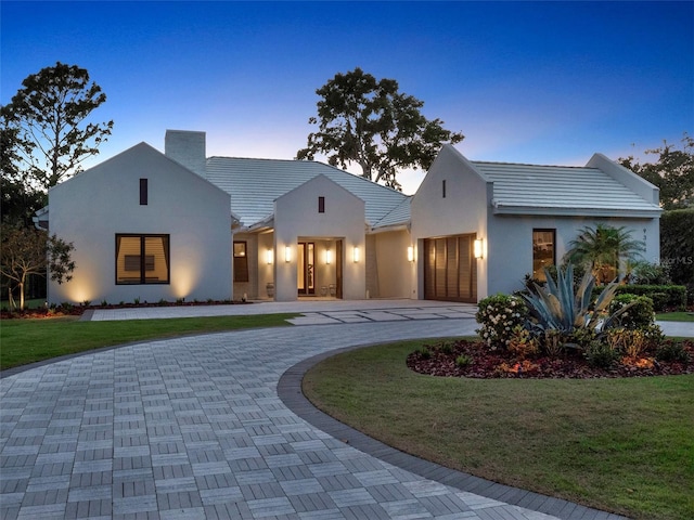 view of front of house featuring stucco siding, curved driveway, a front yard, and a garage