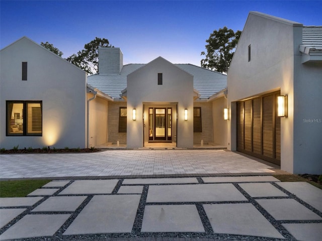 view of front of home with driveway, stucco siding, a tiled roof, and a chimney