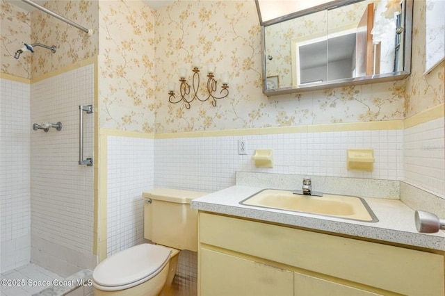 full bath featuring vanity, wallpapered walls, a shower stall, and a wainscoted wall