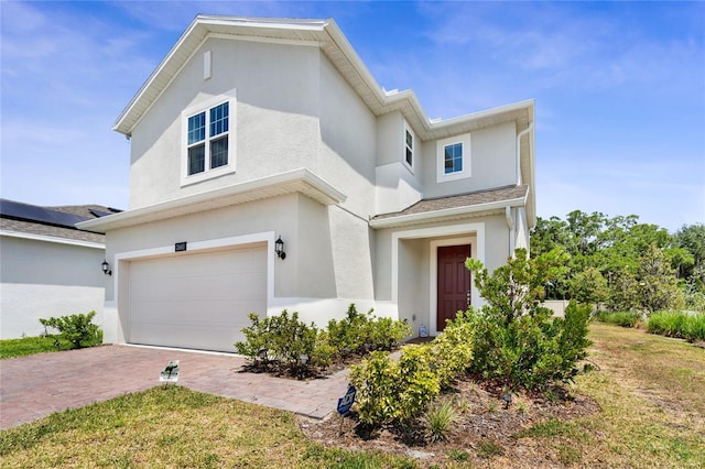 view of front of home with stucco siding, decorative driveway, a front lawn, and a garage