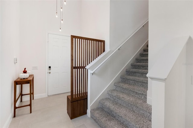 stairway with baseboards, tile patterned flooring, and a towering ceiling