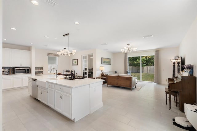 kitchen with appliances with stainless steel finishes, a sink, white cabinets, a notable chandelier, and an island with sink