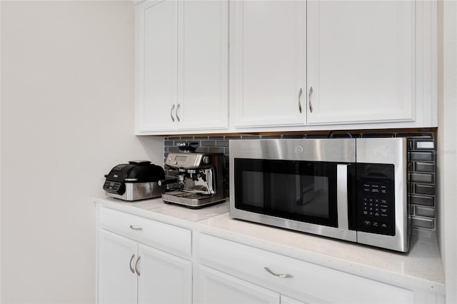 room details featuring white cabinetry, stainless steel microwave, and decorative backsplash