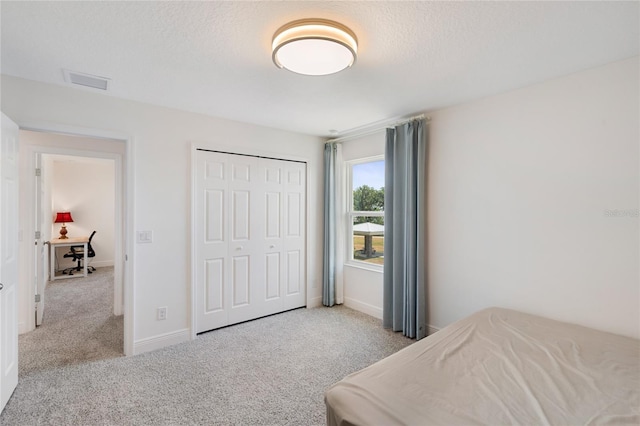 bedroom featuring a textured ceiling, visible vents, carpet, and a closet