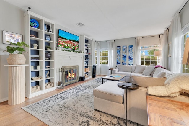 living area featuring visible vents, a glass covered fireplace, wood finished floors, baseboards, and built in shelves