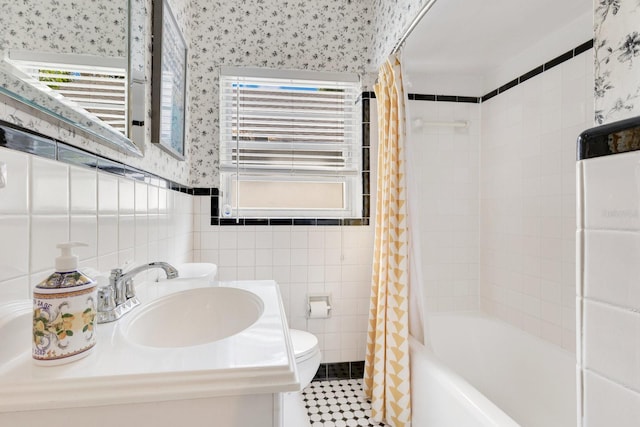 bathroom with a sink, toilet, radiator, wallpapered walls, and tile walls