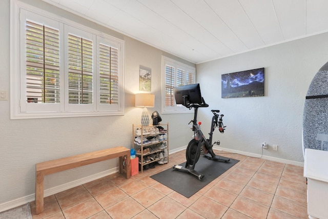 exercise area featuring baseboards, a textured wall, and tile patterned floors