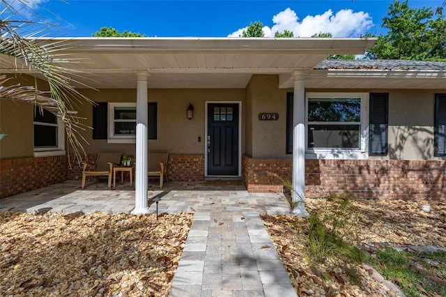 view of exterior entry with covered porch, brick siding, and stucco siding