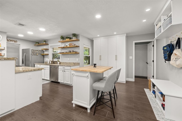 kitchen featuring open shelves, a kitchen breakfast bar, wooden counters, stainless steel appliances, and visible vents