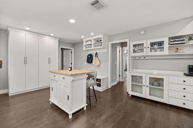 kitchen with open shelves, a breakfast bar area, dark wood finished floors, visible vents, and butcher block counters