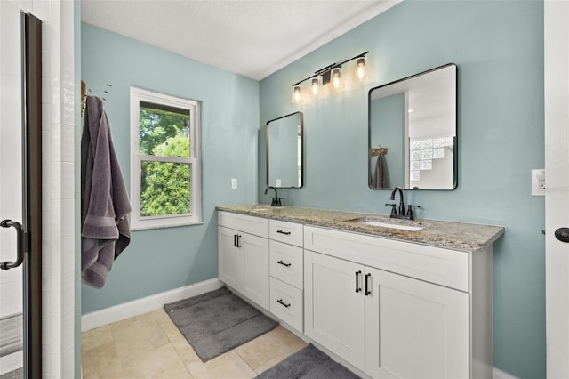 full bath featuring baseboards, a sink, double vanity, and a tile shower