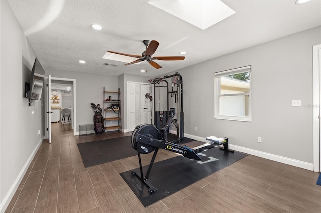exercise room featuring a skylight, baseboards, recessed lighting, and wood finished floors