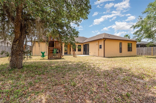 rear view of property featuring stucco siding, a playground, fence, and a yard