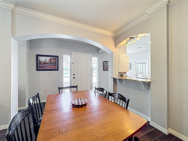 dining room featuring crown molding, arched walkways, baseboards, and a wealth of natural light
