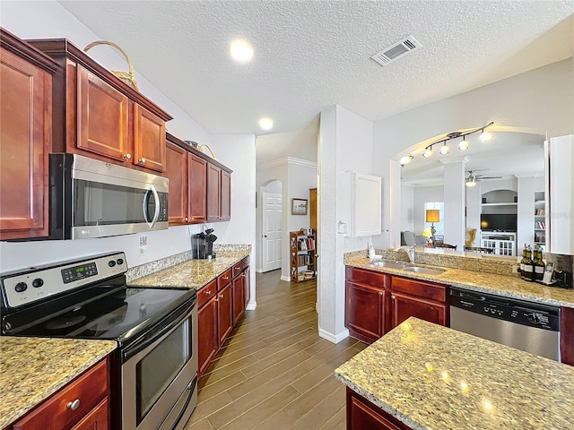 kitchen with stainless steel appliances, arched walkways, a sink, and reddish brown cabinets