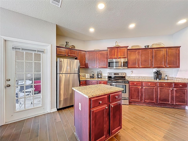 kitchen featuring light stone countertops, appliances with stainless steel finishes, wood finished floors, reddish brown cabinets, and visible vents