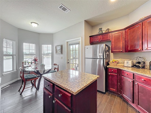 kitchen featuring visible vents, freestanding refrigerator, a kitchen island, reddish brown cabinets, and dark wood-type flooring