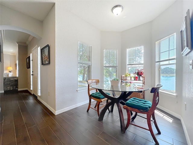 dining room with crown molding, arched walkways, baseboards, and dark wood-style floors