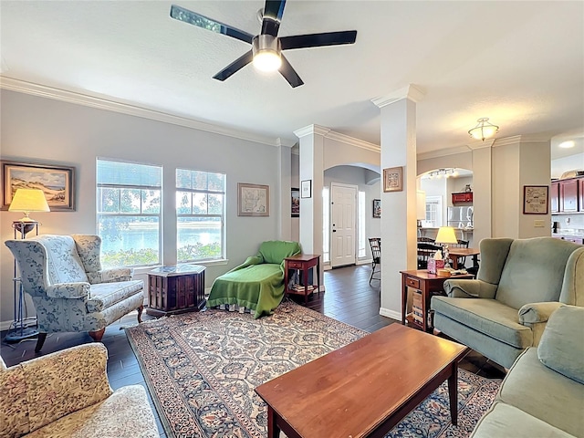 living room with ceiling fan, crown molding, arched walkways, baseboards, and dark wood-type flooring