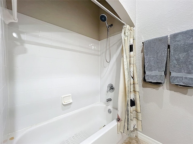 bathroom featuring baseboards, a textured wall, and shower / tub combo