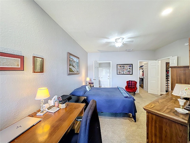 bedroom with a textured wall, light carpet, ceiling fan, a spacious closet, and ensuite bath