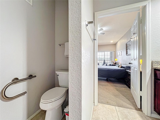 ensuite bathroom featuring tile patterned flooring, vanity, baseboards, toilet, and a textured wall