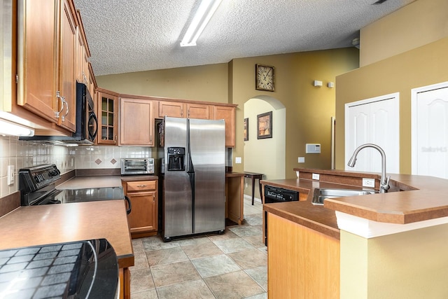 kitchen featuring backsplash, a textured ceiling, arched walkways, a sink, and black appliances