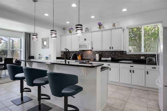 kitchen with a healthy amount of sunlight, dark countertops, a kitchen breakfast bar, and white appliances