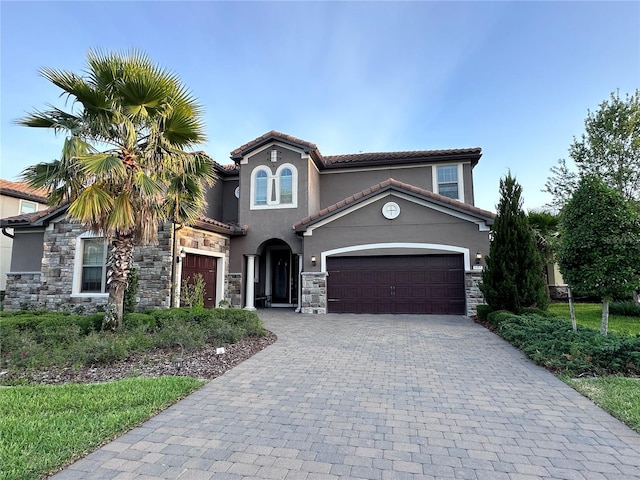 mediterranean / spanish home with stone siding, a garage, stucco siding, decorative driveway, and a tiled roof
