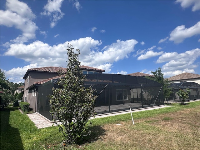 back of house featuring a lawn, glass enclosure, stucco siding, and a tiled roof