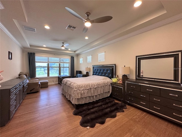 bedroom featuring a tray ceiling, visible vents, ornamental molding, and light wood-style floors