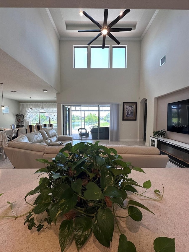 carpeted living room featuring visible vents, crown molding, arched walkways, a high ceiling, and a wealth of natural light