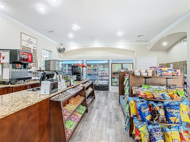 kitchen with crown molding, visible vents, light wood-style floors, light stone counters, and arched walkways