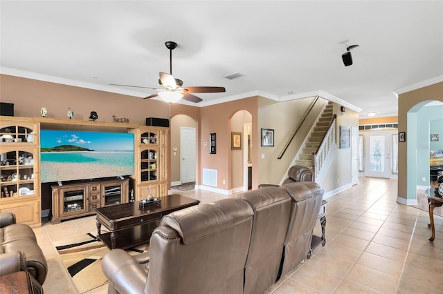 living area featuring a ceiling fan, crown molding, arched walkways, light tile patterned floors, and stairway
