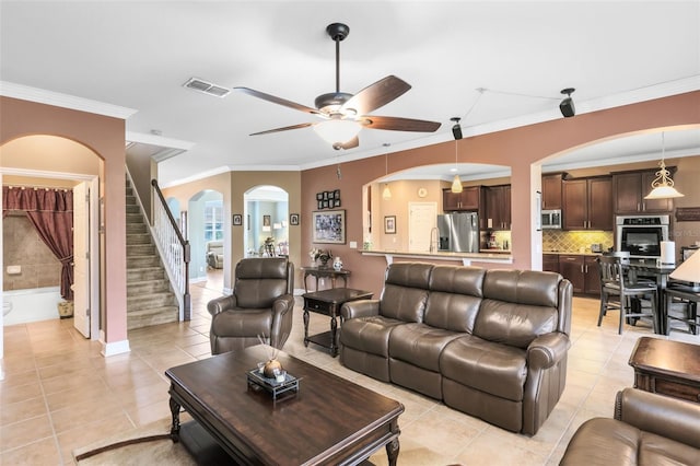living room featuring ceiling fan, visible vents, crown molding, arched walkways, and light tile patterned floors