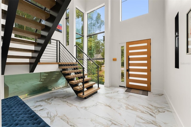 foyer featuring stairs, baseboards, a high ceiling, and marble finish floor