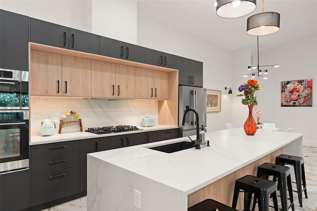 kitchen with a kitchen island with sink, appliances with stainless steel finishes, dark cabinetry, and a sink