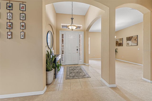 tiled entryway featuring arched walkways, baseboards, and carpet