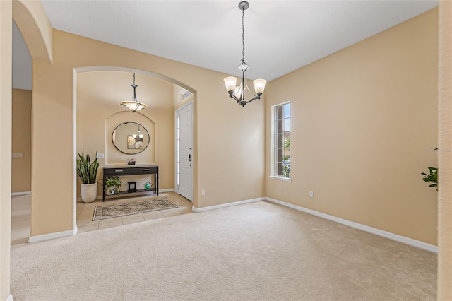 carpeted entrance foyer with arched walkways, baseboards, and a notable chandelier