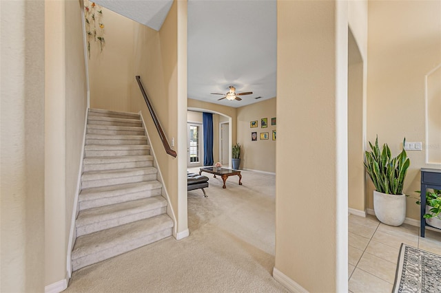 stairway featuring carpet floors, arched walkways, baseboards, and a ceiling fan