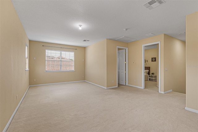empty room with visible vents, attic access, baseboards, and light carpet