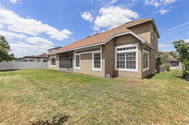 back of property with fence, stucco siding, a sunroom, central AC unit, and a yard