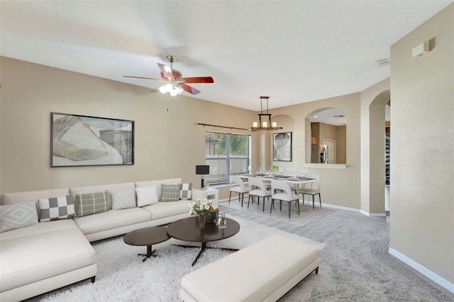 living room featuring carpet flooring, arched walkways, a ceiling fan, baseboards, and a chandelier