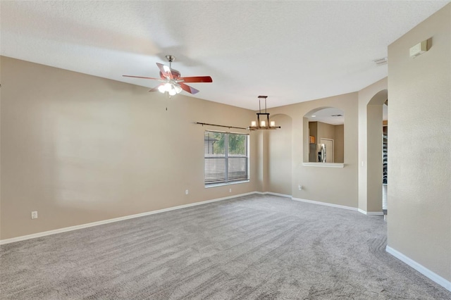 carpeted spare room featuring a ceiling fan, baseboards, arched walkways, and a chandelier
