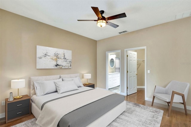 bedroom with wood finished floors, a spacious closet, baseboards, and ensuite bath