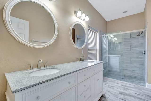 bathroom with a stall shower, double vanity, and wood finished floors