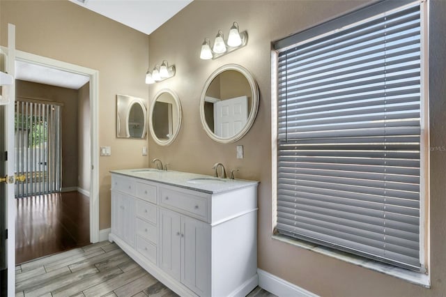 bathroom with baseboards, wood finished floors, and double vanity