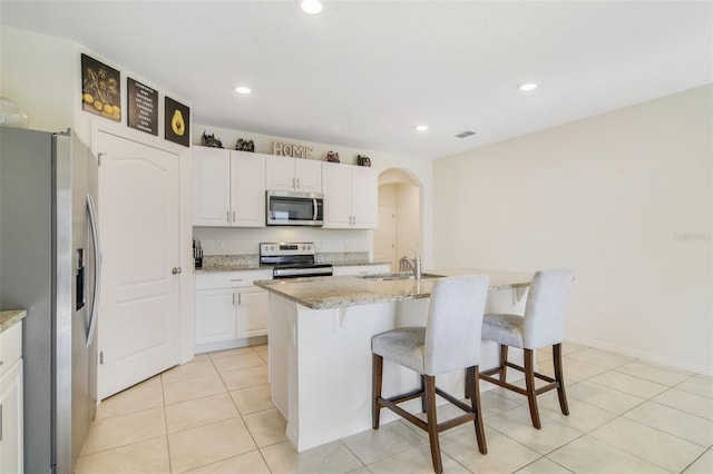 kitchen with stainless steel appliances, a sink, arched walkways, white cabinets, and a kitchen bar