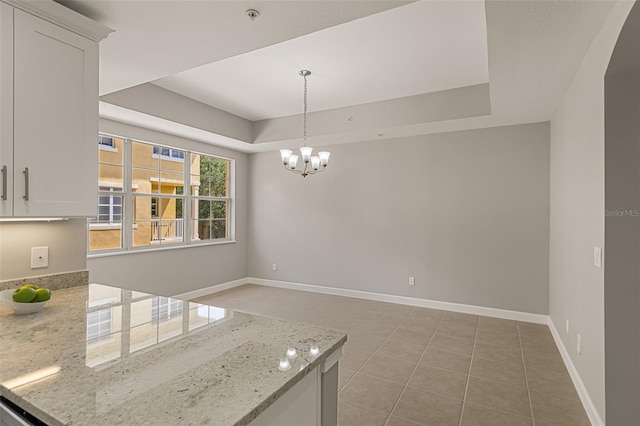 unfurnished dining area featuring a raised ceiling, a chandelier, baseboards, and light tile patterned floors