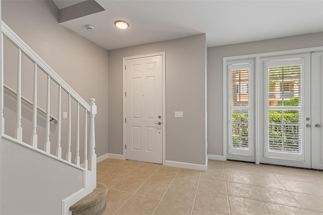 entryway featuring light tile patterned floors, baseboards, and stairs